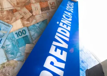 Notas de reais espalhadas ao lado de prédio com placa azul da Previdência Social