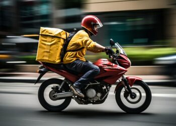 Motociclista entregador com capacete e mochila amarela, em alta velocidade, trabalhando com motocicleta nas ruas.