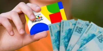Cartão do programa Bolsa Família sendo segurado por uma pessoa ao lado de notas de dinheiro, representando a antecipação do benefício em cidades brasileiras.