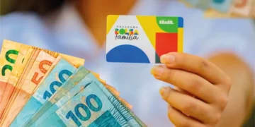 Cartão do Bolsa Família em primeiro plano, com notas de 50, 100 e 200 reais ao fundo, simbolizando a diminuição no número de beneficiários do programa em março de 2026