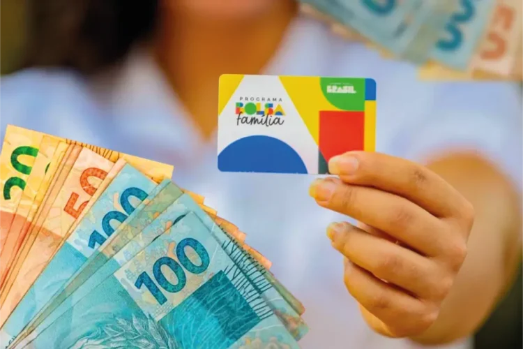 Cartão do Bolsa Família em primeiro plano, com notas de 50, 100 e 200 reais ao fundo, simbolizando a diminuição no número de beneficiários do programa em março de 2026