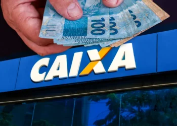 Mão segura cédulas de R$ 100 em frente à fachada da CAIXA