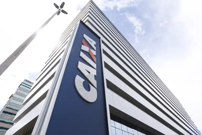 Mais de R$ 6 mil disponíveis na CAIXA: consulte quem pode solicitar o saque a partir desta sexta-feira (13) 2 Prédio moderno da CAIXA visto de baixo com letreiro azul e céu ao fundo