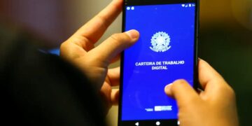 Mãos segurando um smartphone com o aplicativo da Carteira de Trabalho Digital aberto, ilustrando o debate sobre a redução da jornada de trabalho.