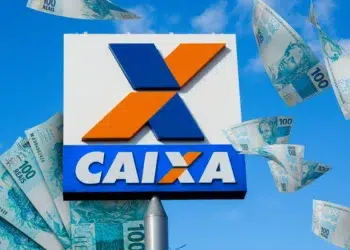 Placa da Caixa Econômica Federal com cédulas de 100 reais ao redor representando saque de R$ 6.220 liberado para moradores do AC, da BA e de MG