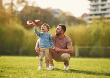 Pai e filho brincando juntos no parque com um avião de brinquedo, representando momentos de qualidade e a importância do vínculo familiar durante a licença-paternidade.