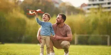 Pai e filho brincando juntos no parque com um avião de brinquedo, representando momentos de qualidade e a importância do vínculo familiar durante a licença-paternidade.