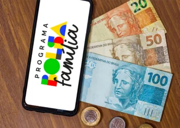 Celular com logo do Programa Bolsa Família apoiado sobre notas de R$ 20, R$ 50 e R$ 100, representando o pagamento do benefício em março de 2026