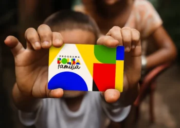 Criança segurando cartão colorido do Programa Bolsa Família com fundo desfocado