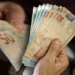 Beneficiário segurando notas de dinheiro relacionadas ao pagamento do BPC de março que começa dia 25 com antecipação em algumas regiões.
