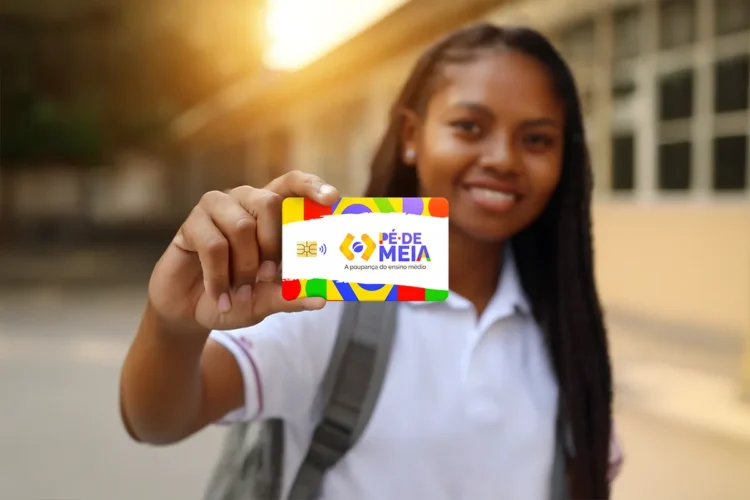 Pé-de-Meia finaliza pagamentos de março nesta segunda-feira (30) — saiba quando será o próximo depósito? 2 Jovem segura cartão colorido do Pé-de-Meia com sorriso em frente à escola