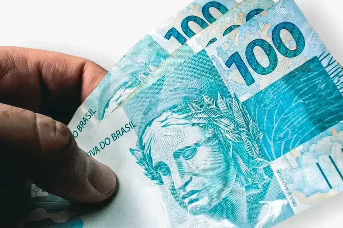 Nova proposta busca garantir piso de R$ 2.750 para trabalhadores do comércio 2 Notas de R$100 em mãos simbolizando piso salarial de R$2.500 a R$2.750 para trabalhadores do comércio no Brasil.