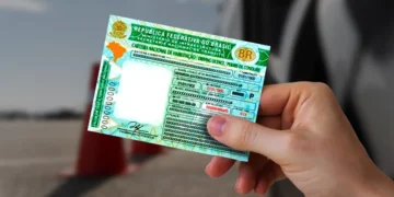 Uma pessoa segurando a CNH brasileira com informações pessoais ocultas, em fundo de cones de trânsito.