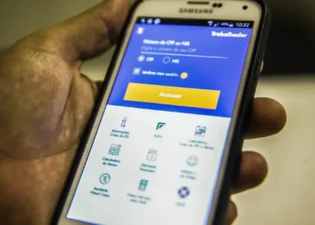 Mão segurando celular com aplicativo do Trabalhador aberto, canal oficial para solicitar o Saque Calamidade do FGTS de até R$ 6.220 pelo smartphone