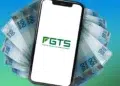 Smartphone exibe logo do FGTS cercado por notas de R$ 100 sobre fundo azul e verde gradiente.