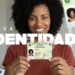 Mulher negra sorrindo mostra a CIN com foto 3x4, brasão e texto "Nova Identidade" ao fundo