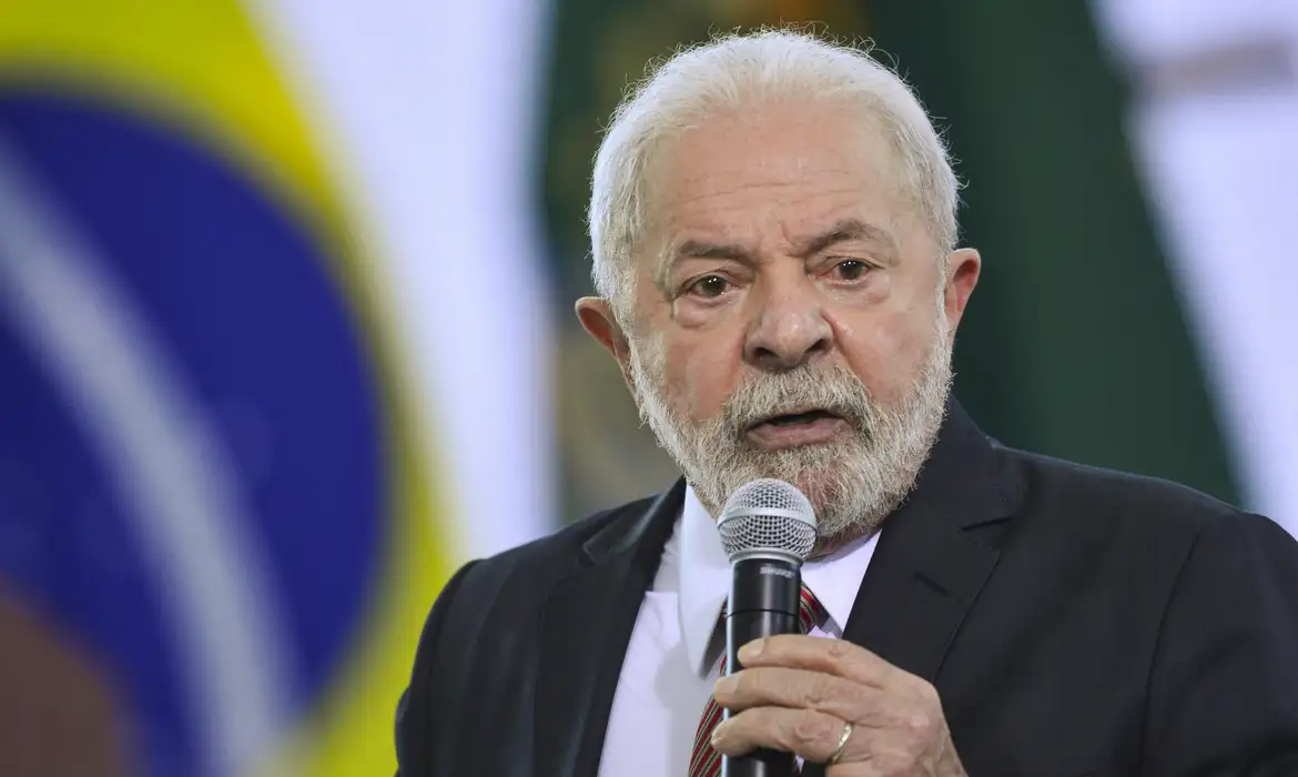 Lula afirma que projeto sobre o fim da escala 6×1 será enviado ao Congresso e diz ter certeza de aprovação 2 Presidente Lula discursa com microfone em frente à bandeira do Brasil, vestindo terno escuro e gravata listrada