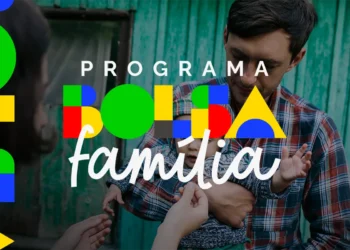 Pai segura criança no colo com logotipo colorido do Programa Bolsa Família sobreposto à imagem.