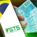 Mão segurando celular com aplicativo FGTS e bandeira do Brasil ao lado de cédulas de R$ 100.