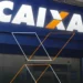 Letreiro Caixa em destaque acima da entrada de agência bancária azul